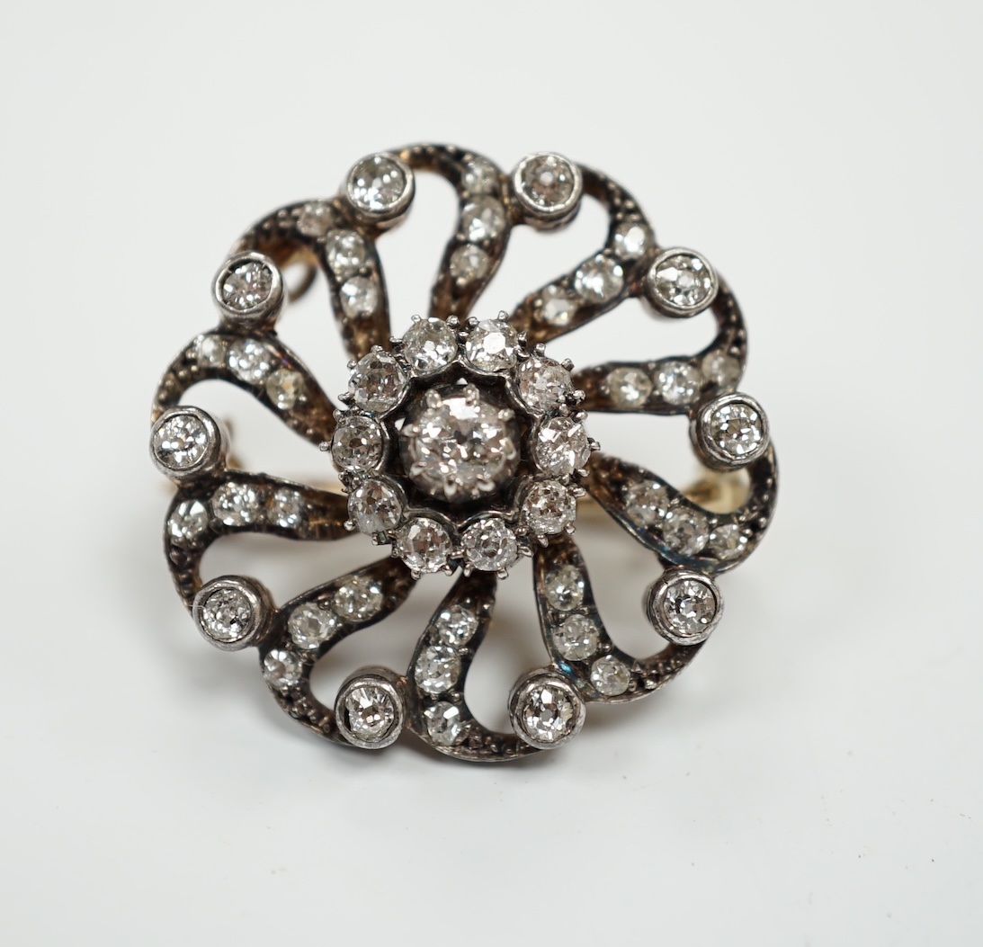 A Victorian yellow metal and diamond cluster set whorl shaped brooch, scrolling border and detachable brooch attachment, 25mm, gross weight 8.7 grams.